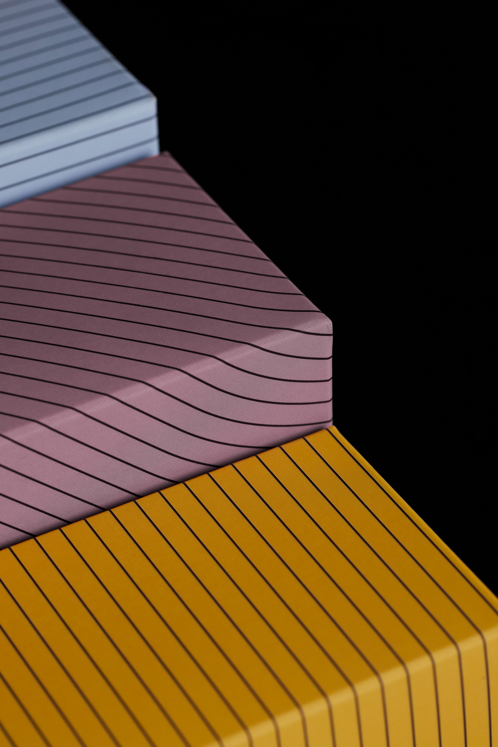 Abstract close-up of three horizontally stacked blocks in shades of yellow, pink, and blue, each featuring parallel black stripes.