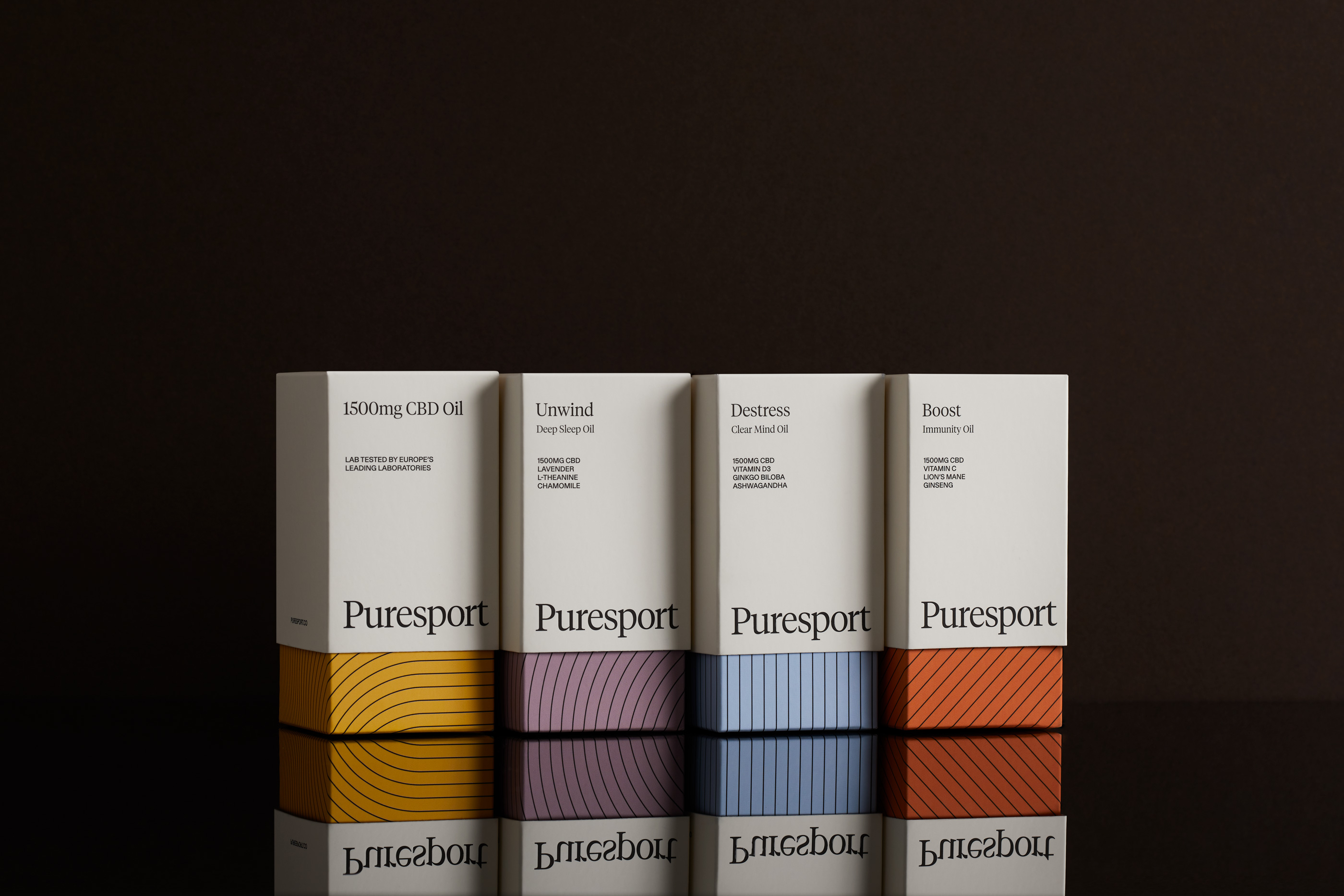 Four Puresport CBD oil product boxes in a studio shot against a dark background with reflective surface showcasing yellow, purple, blue, and orange designs.