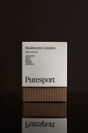 Puresport Mushroom Complex supplement box with a fluted brown base on a reflective dark surface.