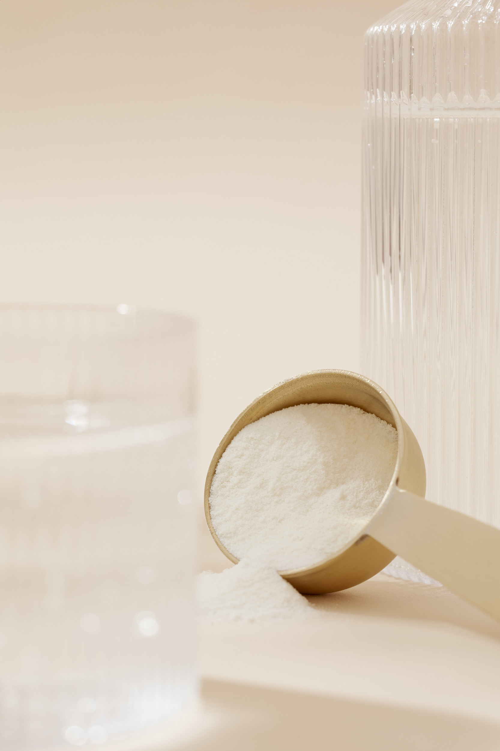 Powder supplement in a golden scoop with a clear glass of water and a ribbed jar in a minimalist, neutral setting. Health and wellness.