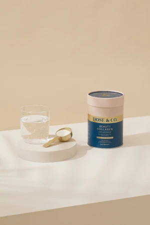 Product shot of Dose & Co. Beauty Collagen supplement with a scoop and glass of water, featuring a clean, minimalist aesthetic.