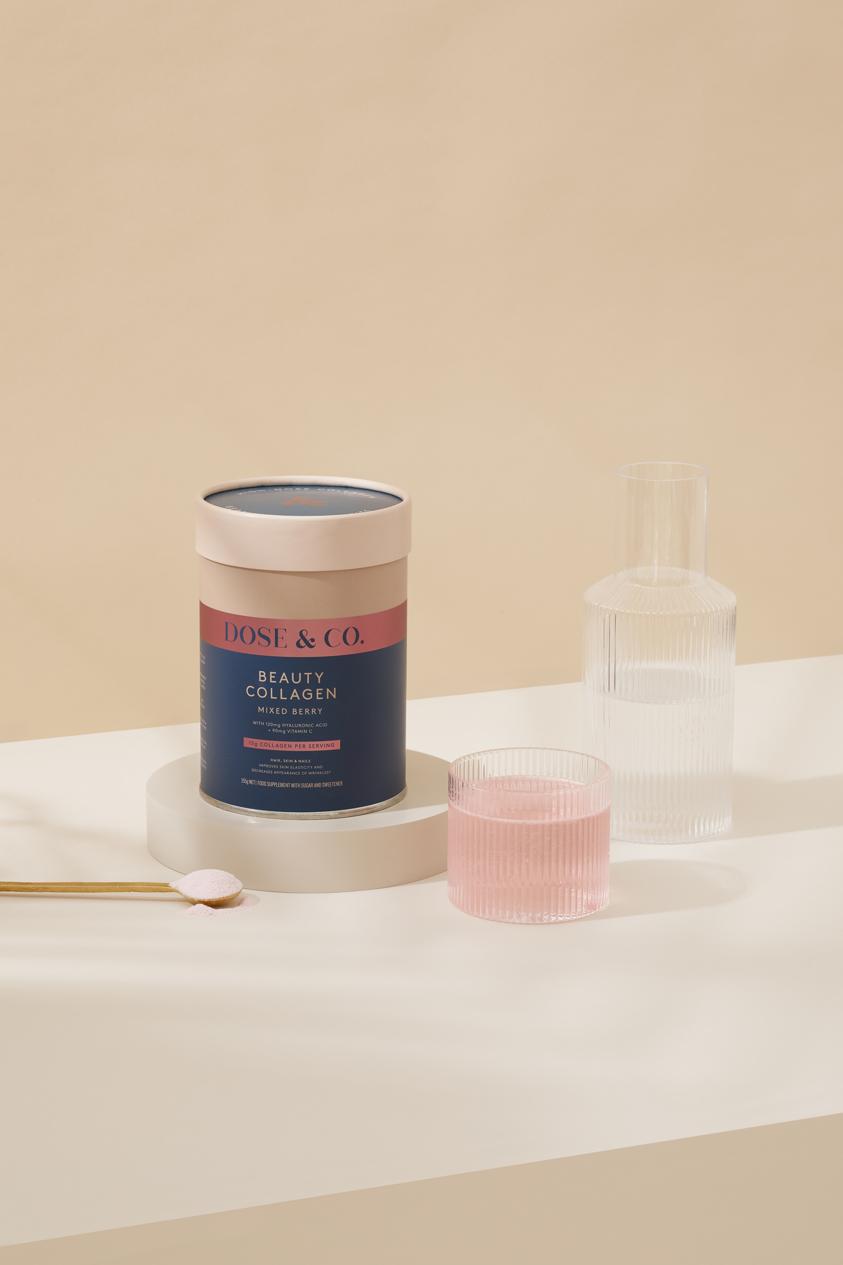 Dose & Co. beauty collagen can on a concrete stand with a glass of liquid and a golden spoon with powder, studio shot.