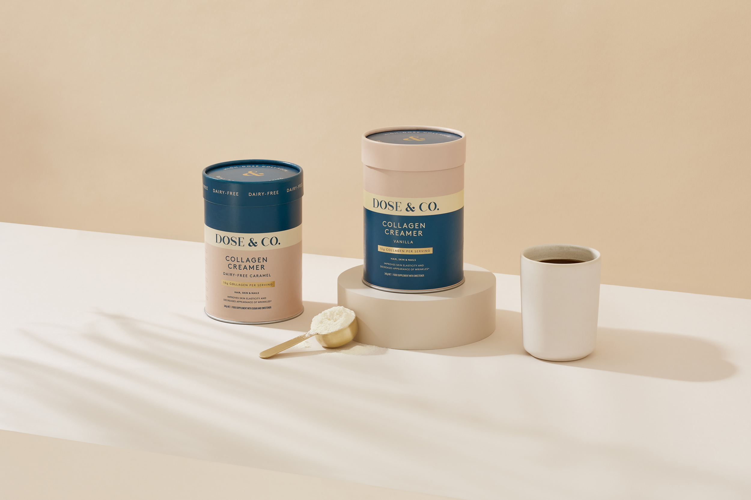 Two Dose & Co. collagen creamers, one cup of coffee, and one scoop of collagen powder are arranged on a white surface.