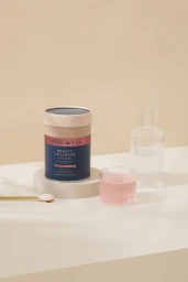 Dose and Co Beauty Collagen Mixed Berry tub on a podium next to a fluted glass with pink liquid and a glass carafe.