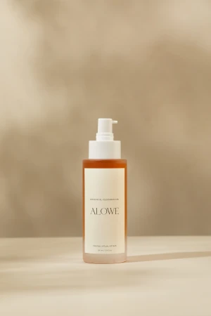 A bottle of Alowe skincare botanical cleansing oil with a white pump dispenser against a warm beige background.