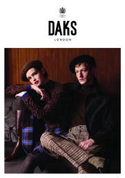 A woman and a man seated together indoors wearing berets, patterned knitwear, and tailored trousers for the Daks campaign.