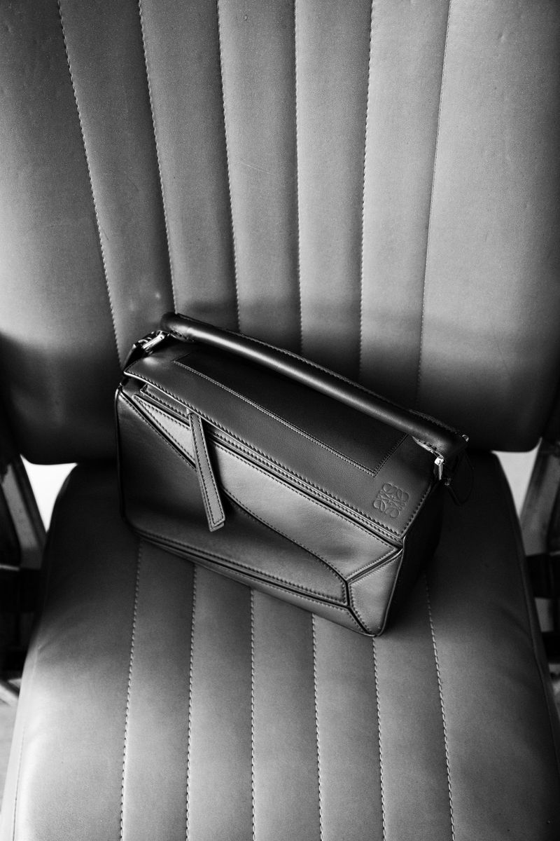 Black leather handbag with geometric design and top handle, placed on a ridged grey chair in a close-up studio shot, luxury, and fashion.