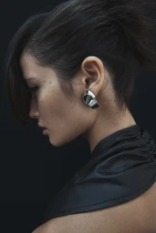 Profile portrait of a woman wearing a metallic silver earring and dark top against a dark background for Mimco.