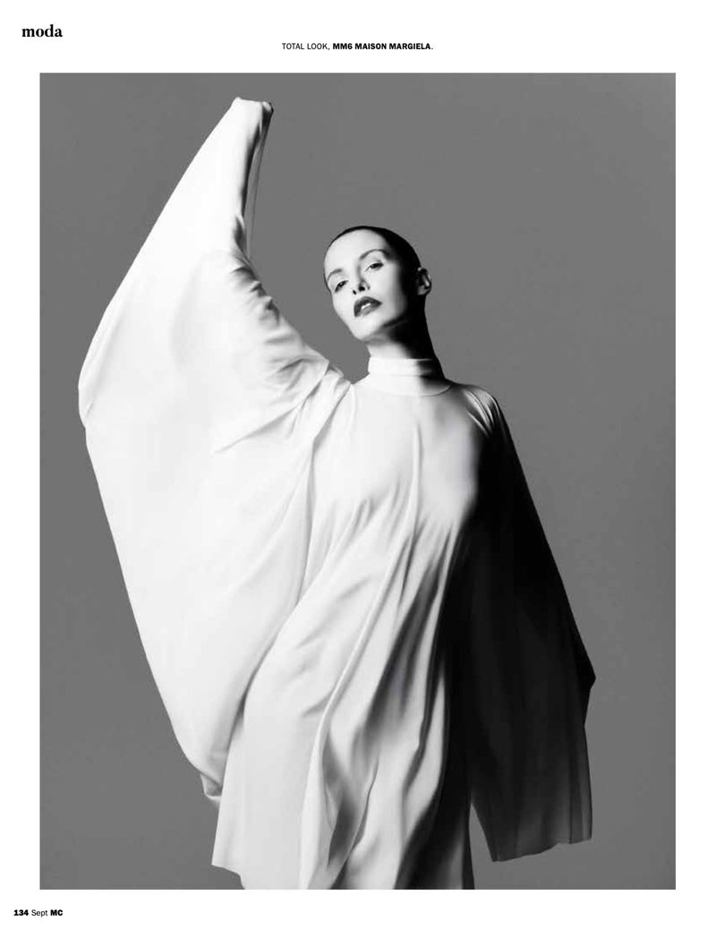 Monochrome fashion shot of a woman in a draped white dress against a grey background, minimalist style, for editorial use.