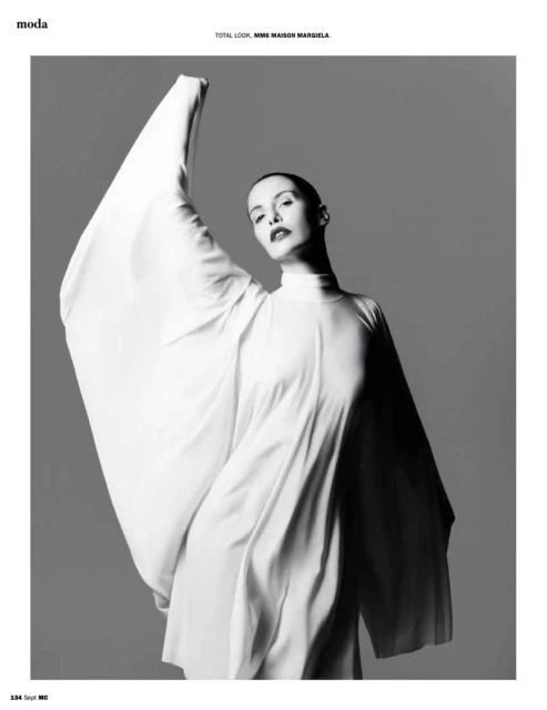 Monochrome fashion shot of a woman in a draped white dress against a grey background, minimalist style, for editorial use.