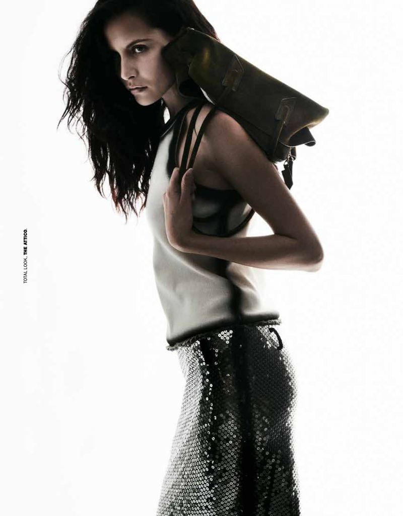 Fashion editorial shot of a woman in a white top and sequined skirt with a leather bag slung over her shoulder against a white backdrop.
