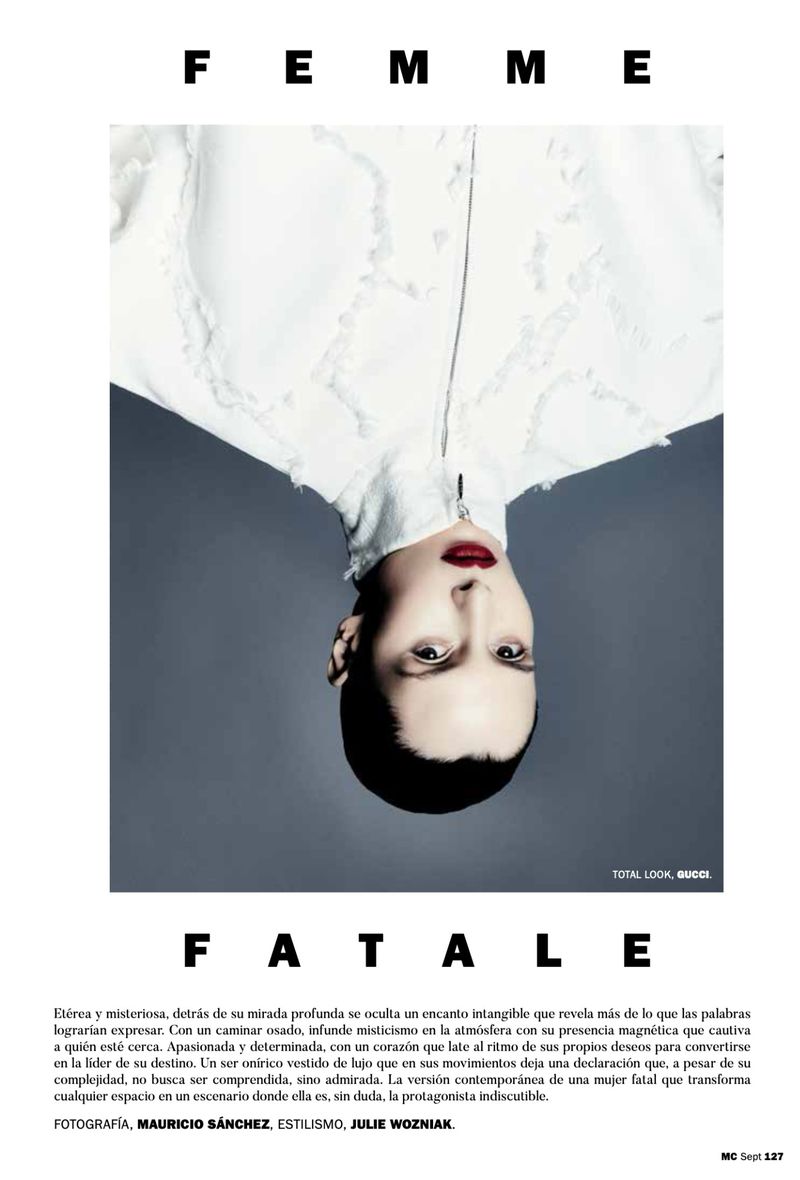 Fashion editorial portrait of a woman with red lipstick and a white textured jacket, posed upside down against a grey background.
