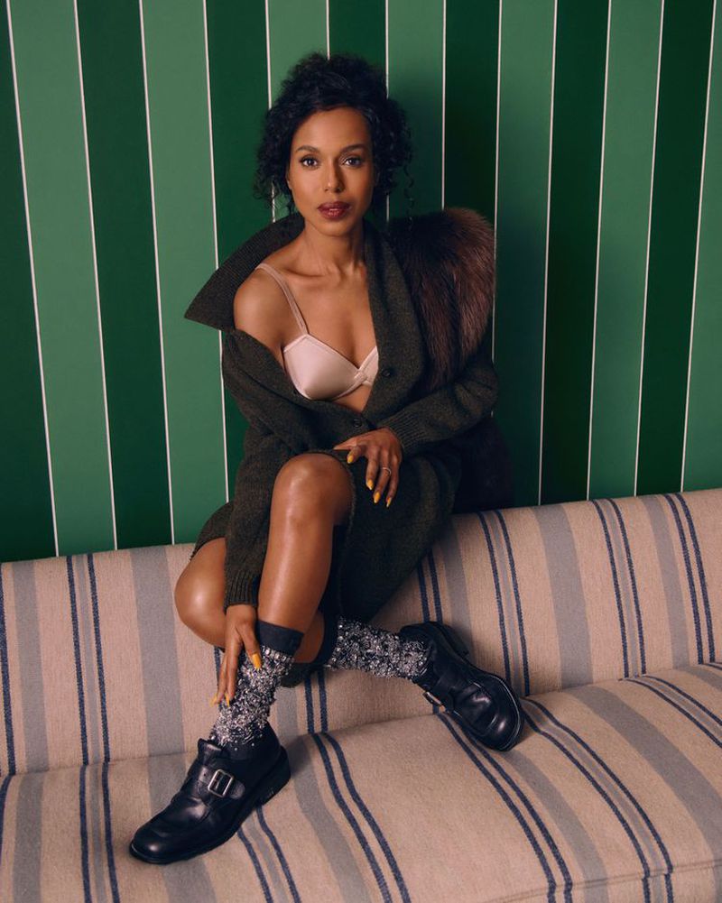 A stylish woman with dark hair sits on a striped couch wearing a coat with fur collar, bra, patterned socks, and buckle shoes.