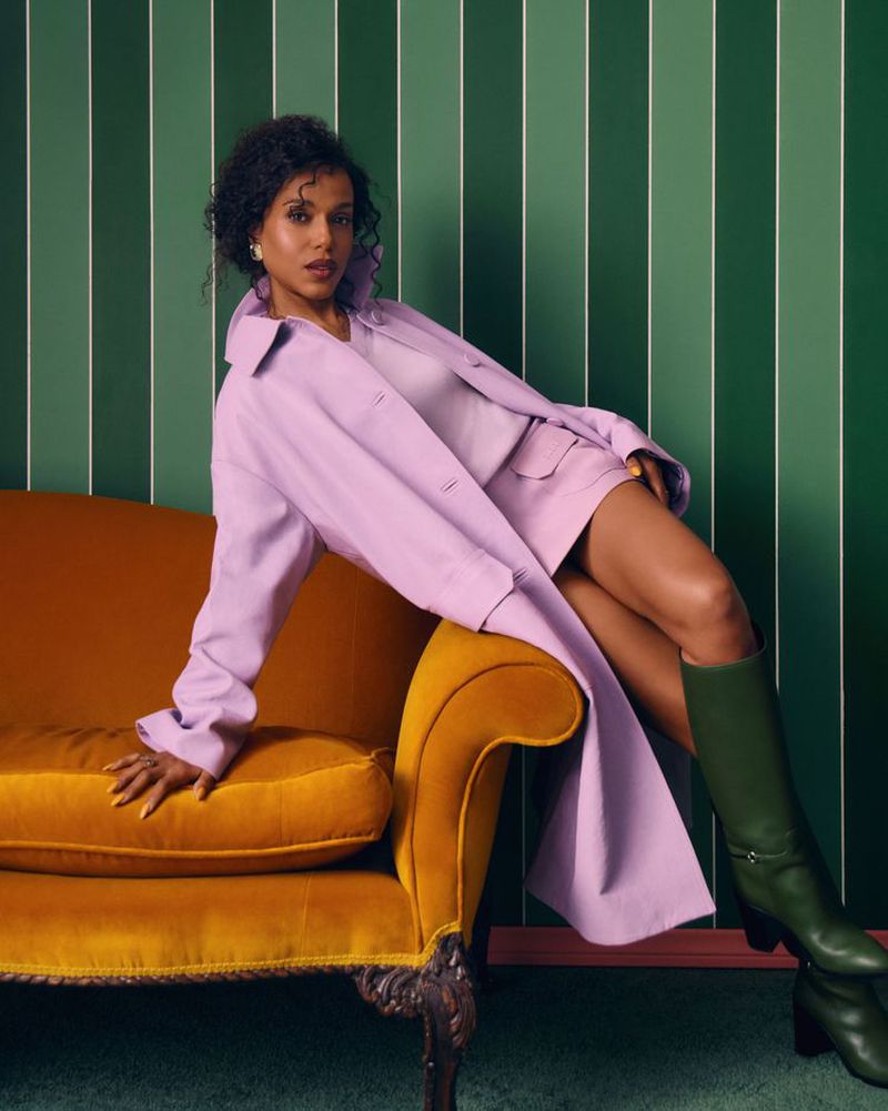 A woman in a lilac outfit poses on a mustard-colored sofa in front of a green and white striped wall, showcasing fashion and style.