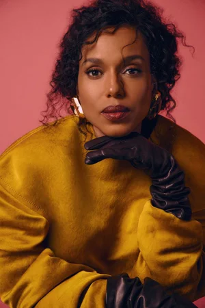 Kerry Washington wearing a mustard yellow top and dark gloves against a pink backdrop