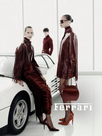 Three models wearing glossy burgundy leather outfits pose around a classic white sports car in a high-key white studio setting.