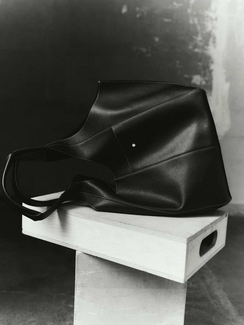 Monochromatic shot of a black leather tote bag with short handles placed on top of two stacked wooden crates in a studio setting.