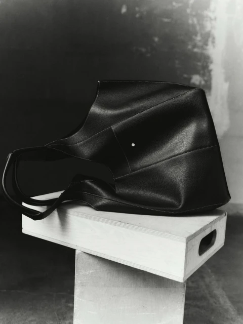 Monochromatic shot of a black leather tote bag with short handles placed on top of two stacked wooden crates in a studio setting.