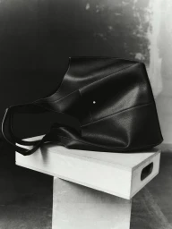 Black structured leather handbag resting on a wooden box against a textured studio background.