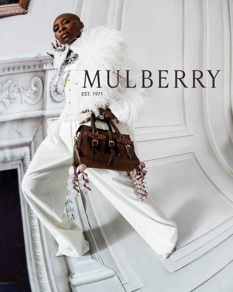 Fashion-forward woman showcases a brown leather Mulberry handbag in a stylish studio setting, emphasizing luxury and brand heritage.