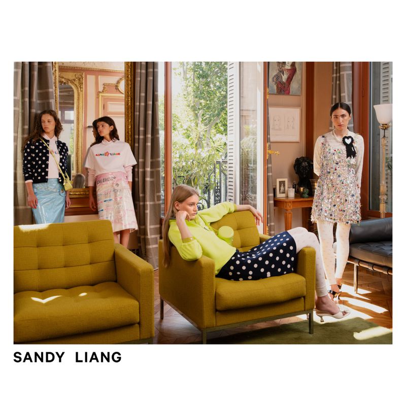 Fashion editorial photo of four women in colorful outfits posing indoors with sofas, window light, hardwood floors, and ornate details.