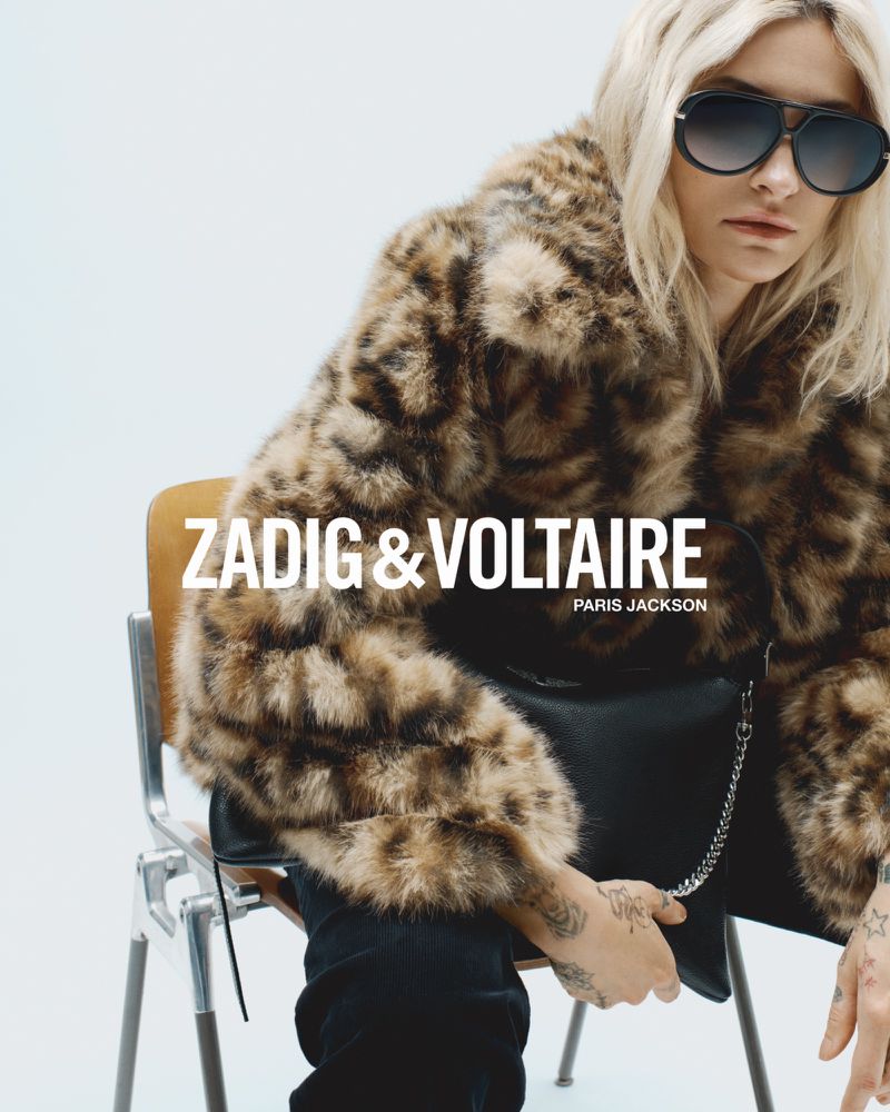An adult female sits on a chair in a fur coat and sunglasses, with a purse, branded Zadig & Voltaire, studio shot on white backdrop.