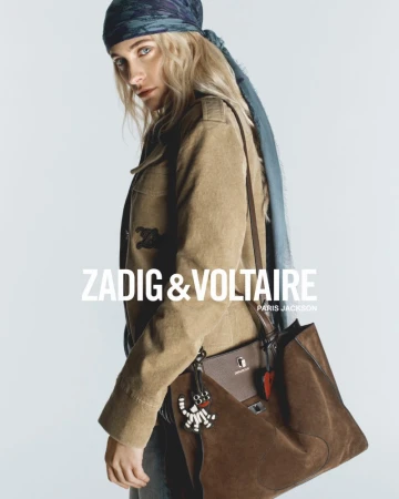 Adult female model wears a headscarf and light brown jacket with a Zadig & Voltaire bag on a white background in a studio shot.