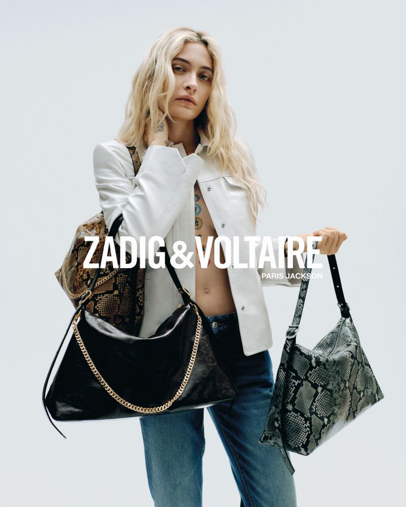 Fashion editorial shot of a blonde woman holding two handbags from Zadig & Voltaire in a white studio, wearing a jacket and jeans.