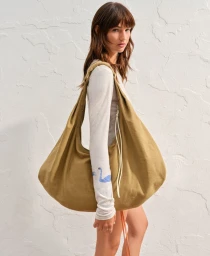 Model Mia Regan carrying a large khaki shoulder bag against a textured white wall for H&M