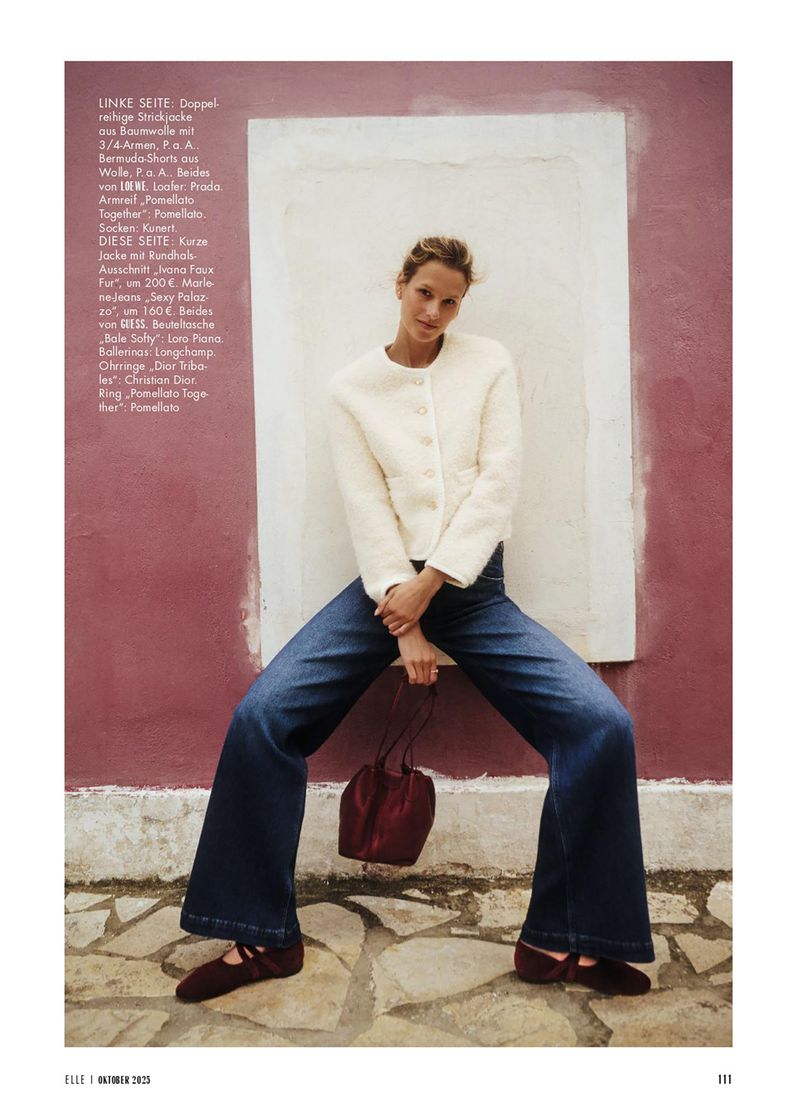Fashion editorial shot of a model in jeans and a fuzzy jacket, standing against a painted wall with a maroon purse. 