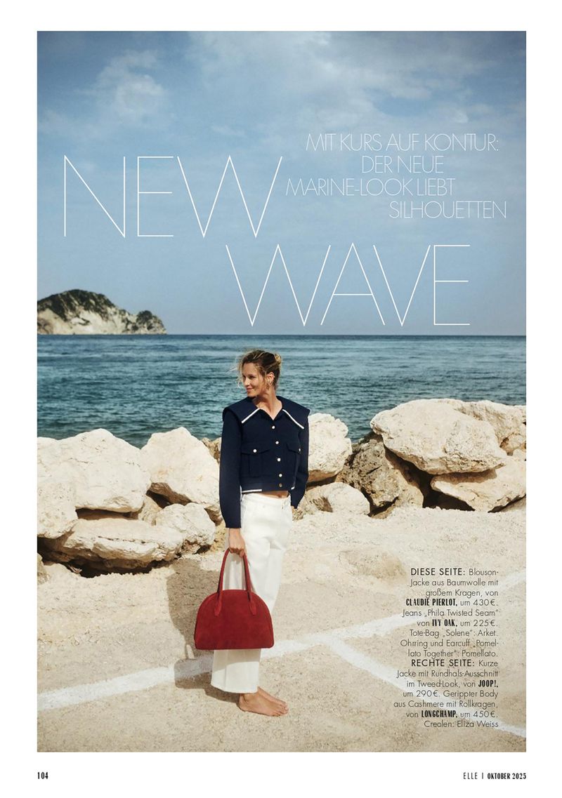 Fashion editorial shot of a woman in a navy jacket and white trousers by the sea, holding a red bag with text overlay.