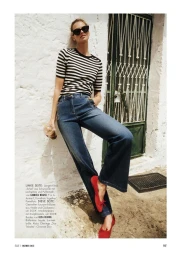Mariina Keskitalo wearing a striped knit top, wide-leg blue jeans, and red ballet flats while leaning against a white stucco wall.