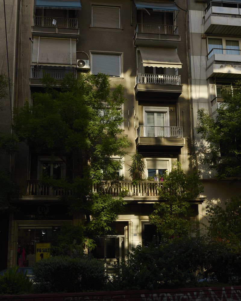 Exterior daytime shot of a weathered multi-story apartment building with balconies and greenery, capturing urban architecture.