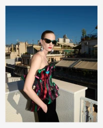 Model Ros Georgiou wearing a ruffled multicolored top and sunglasses on a sunny rooftop for Grazia Germany.