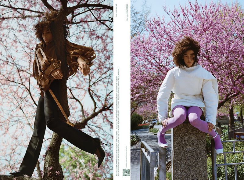 Fashion editorial shot with a young adult model in stylish outerwear, against a backdrop of blooming pink trees, on a sunny day.