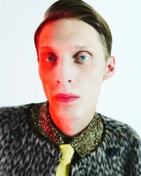 Close-up portrait of a male model with blue eyes wearing a leopard print jacket and yellow tie under red split studio lighting.