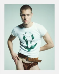 Male model in a white graphic t-shirt, brown leather belt, and leopard print briefs posing against a pale background.