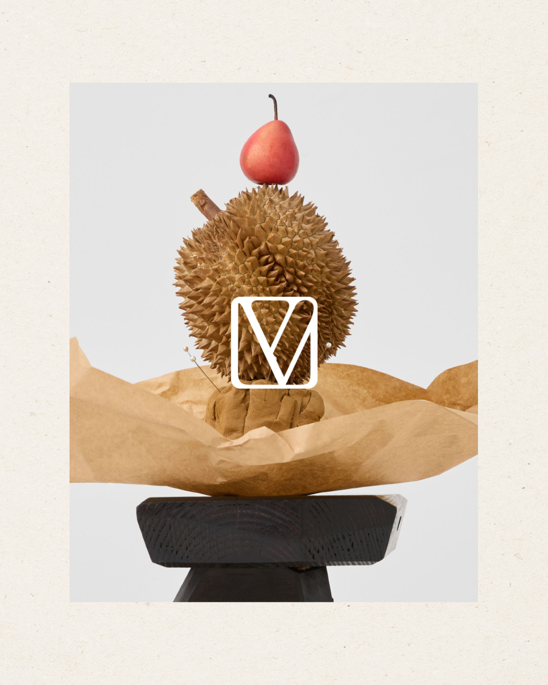 Still life featuring a durian topped with a pear, displayed on a dark wood stool against a light backdrop. Food photography.