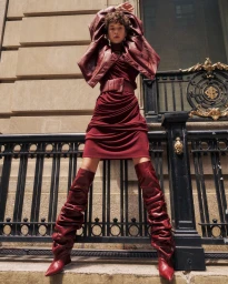 Model Madeleine German posing in a monochromatic burgundy draped dress and slouchy thigh-high boots against an ornate black iron fence.