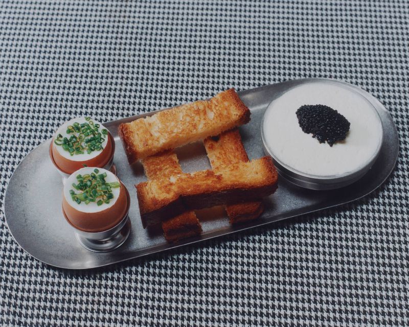 Overhead food photography: toast fingers, eggs topped with scallions, and caviar with cream, arranged on a silver platter.