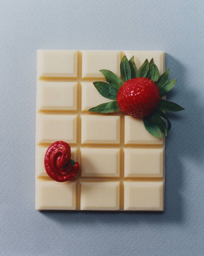 Overhead studio shot of a white chocolate bar adorned with fresh strawberry and red filling against a pale blue backdrop.
