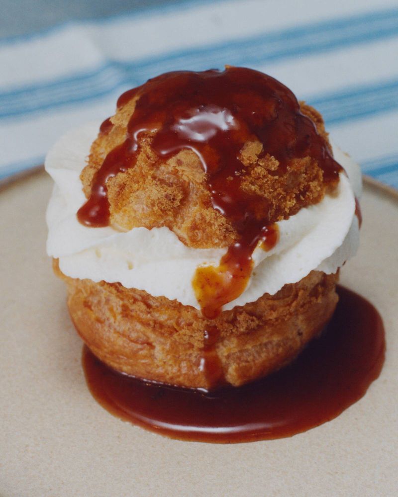 A cream puff dessert on a plate, topped with white cream and brown caramel sauce, showcasing a sweet treat with a pastry base.
