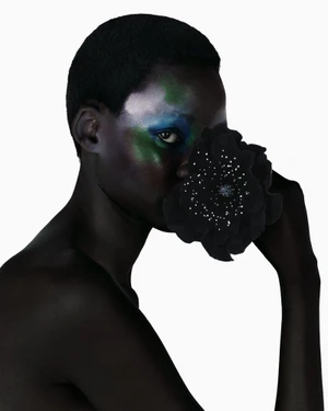 Model with painted face holding a dark flower covering part of her face against a white background