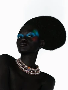 Model Caren Jepkemei with an oversized rounded afro and vibrant blue eye makeup wearing an ornate jeweled collar necklace.