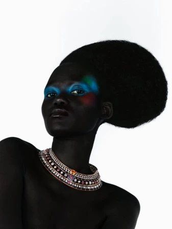 Model Caren Jepkemei with an oversized rounded afro and vibrant blue eye makeup wearing an ornate jeweled collar necklace.
