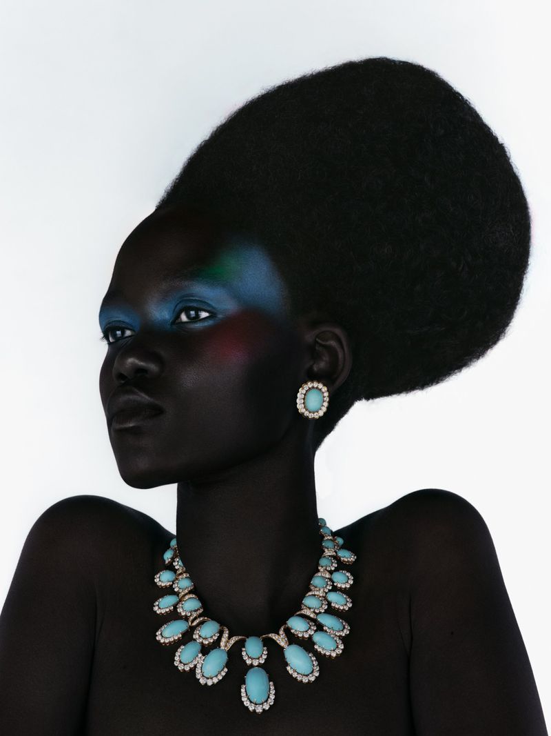 Stunning portrait of a Black woman with dramatic makeup and hair, wearing a turquoise statement necklace and matching earrings against white.