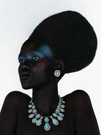 Stunning portrait of a Black woman with dramatic makeup and hair, wearing a turquoise statement necklace and matching earrings against white.