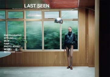 Model in a black jacket and sheer tights standing in a wood-paneled room with large windows and an arched floor lamp.