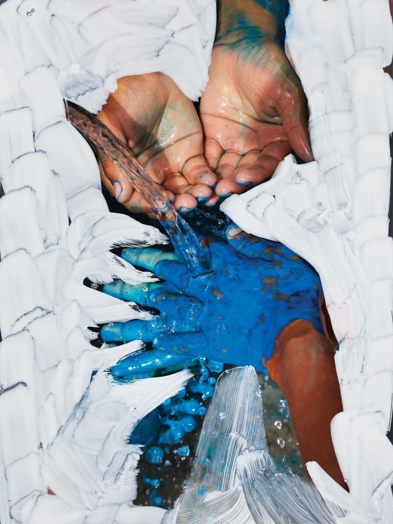 Person washing blue paint from their hands with water. Hands are framed by brushstrokes of thick white paint on a dark surface.