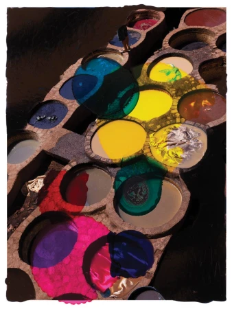 Aerial view of colorful dye vats in a tannery with a person standing on the edge of the dye pits, outdoor, brown and blue colors.